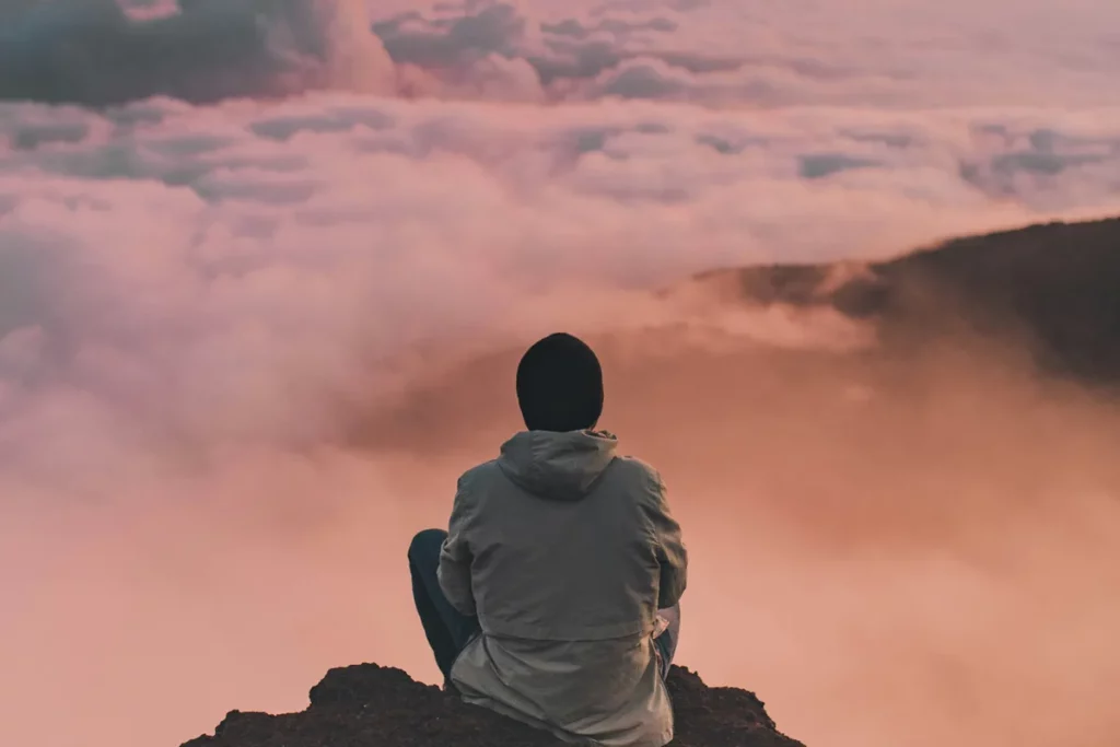 Personne assise de dos contemplant une mer de nuages, image de calme et de lâcher-prise