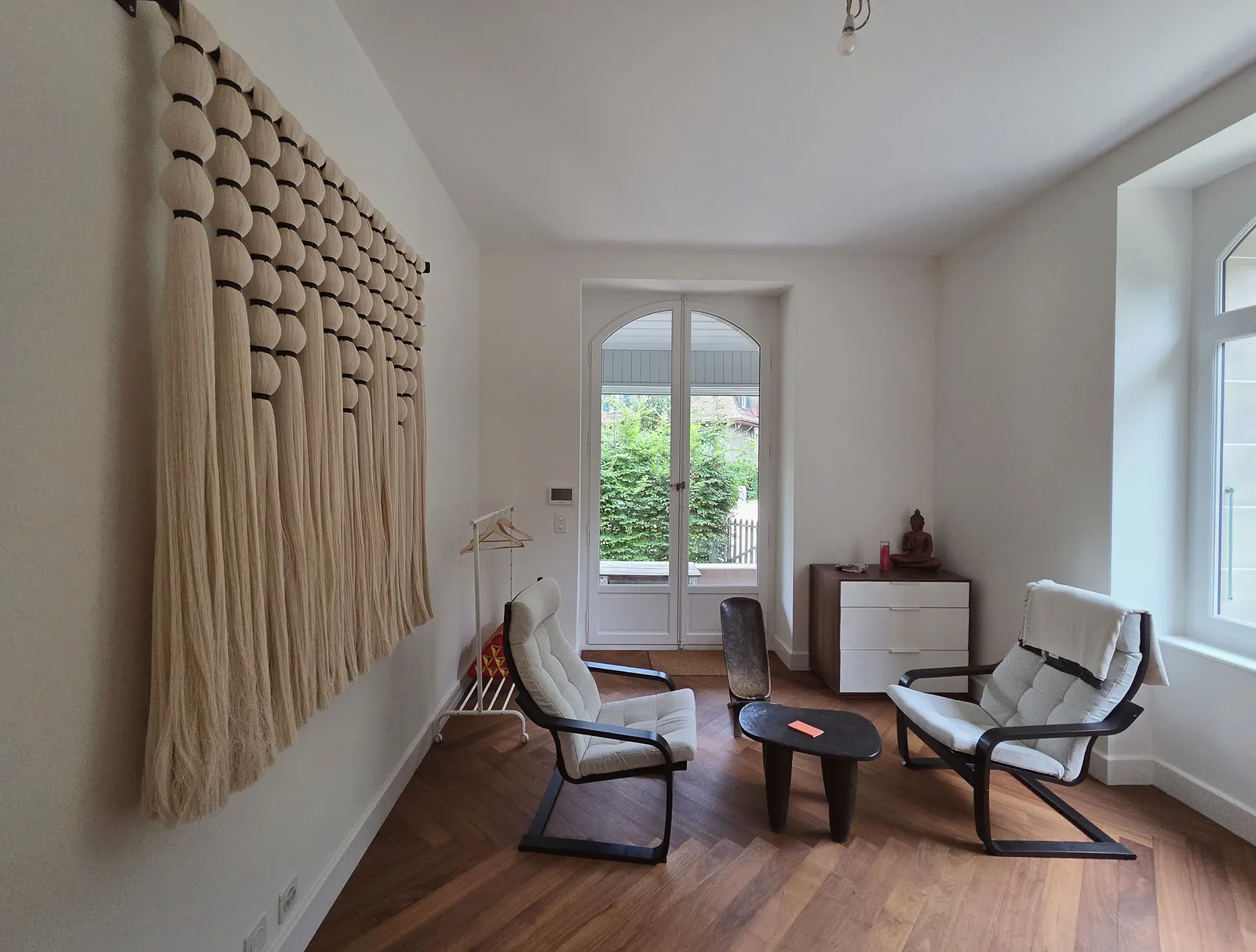 Salle de thérapie du cabinet d'hypnose HypnoVibes à Lausanne, avec ses deux fauteuils inclinables et une grande tenture en macramé